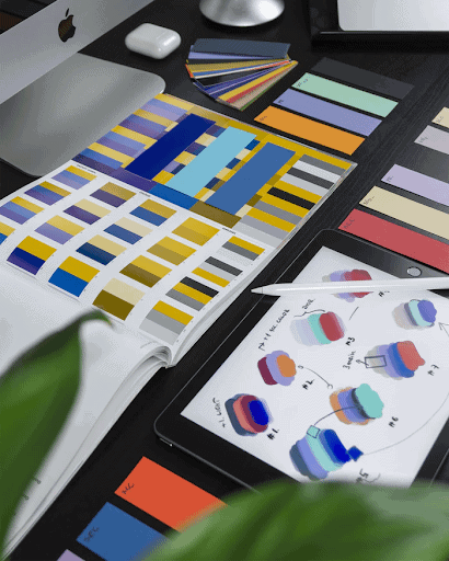 A home office desk with various color swatches in a book, as well as a tablet with a pencil.
